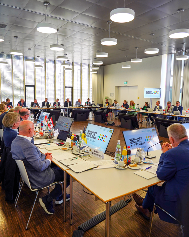 Blick in einen Tagungsraum, in dem Tische zu einem großen Rechteck aufgebaut sind. An den Tischen sitzen die Besprechungsteilnehmer