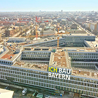 München aus der Vogelperspektive. Im Vordergrund die Baustelle für das neue Justizzentrum. Darauf ist der Schriftzug "Ich bau Bayern" eingeblendet.
